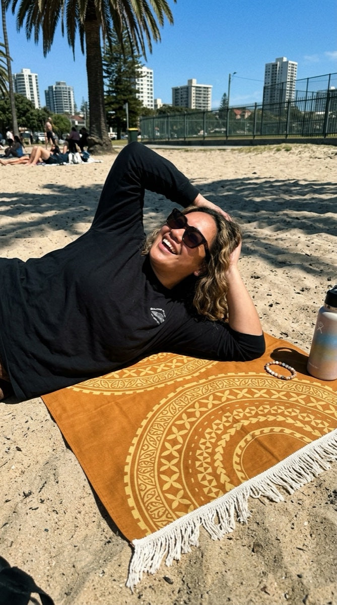 Golden Sun MWW on Demand multipurpose lavalava displayed as a vibrant beach towel with tropical patterns on a sandy beach.